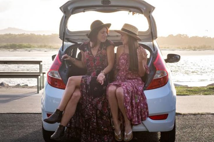 Two girls sitting in the back of a JUCY car at the beach
